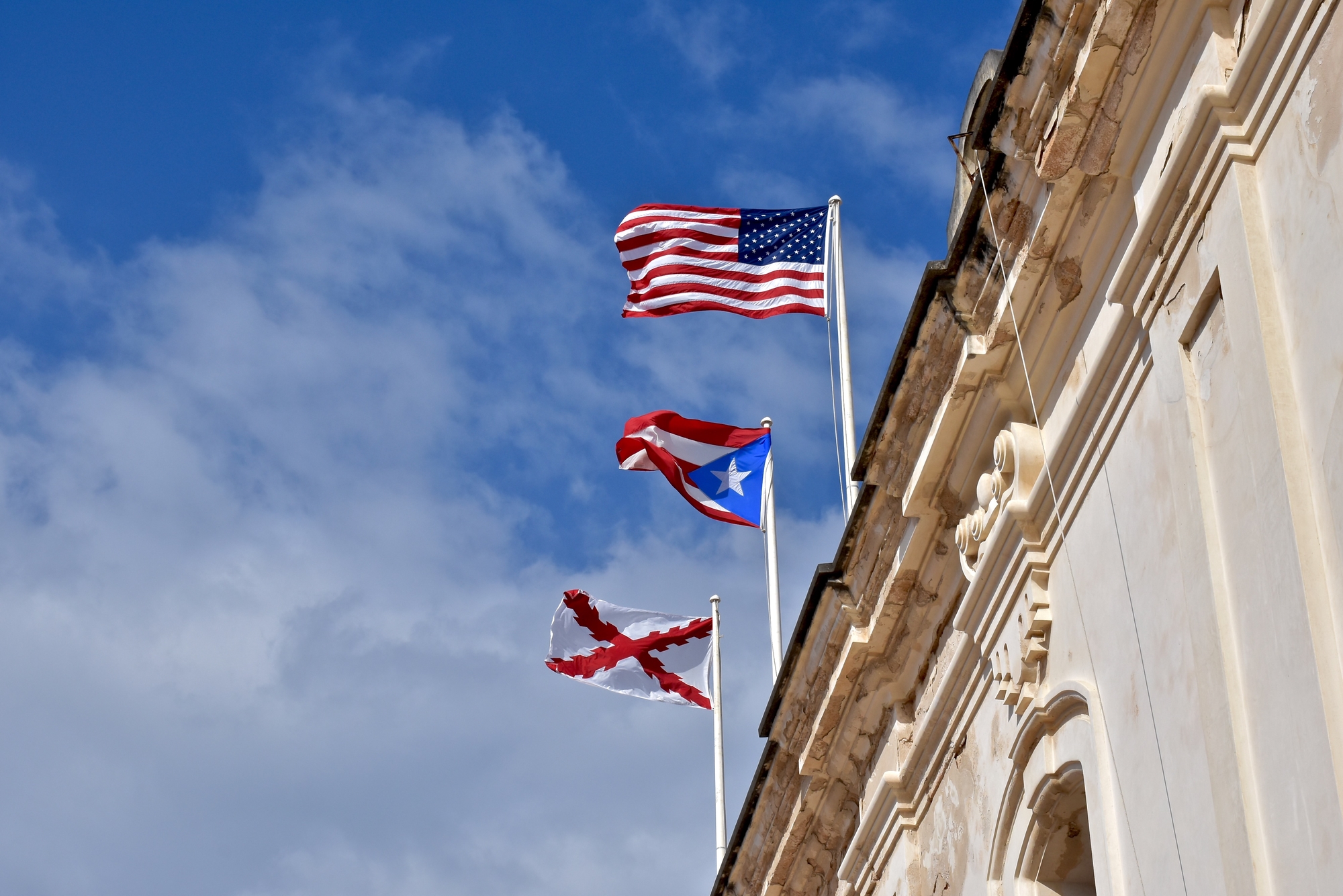 The American flag flies over the flag of Puerto Rico on top of a colonial building